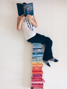 Man sits reading on pile of books. Photo by Merve Bayar from Pexels